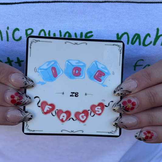 "NICE IS FIGS" sticker held by woman with red and black nails